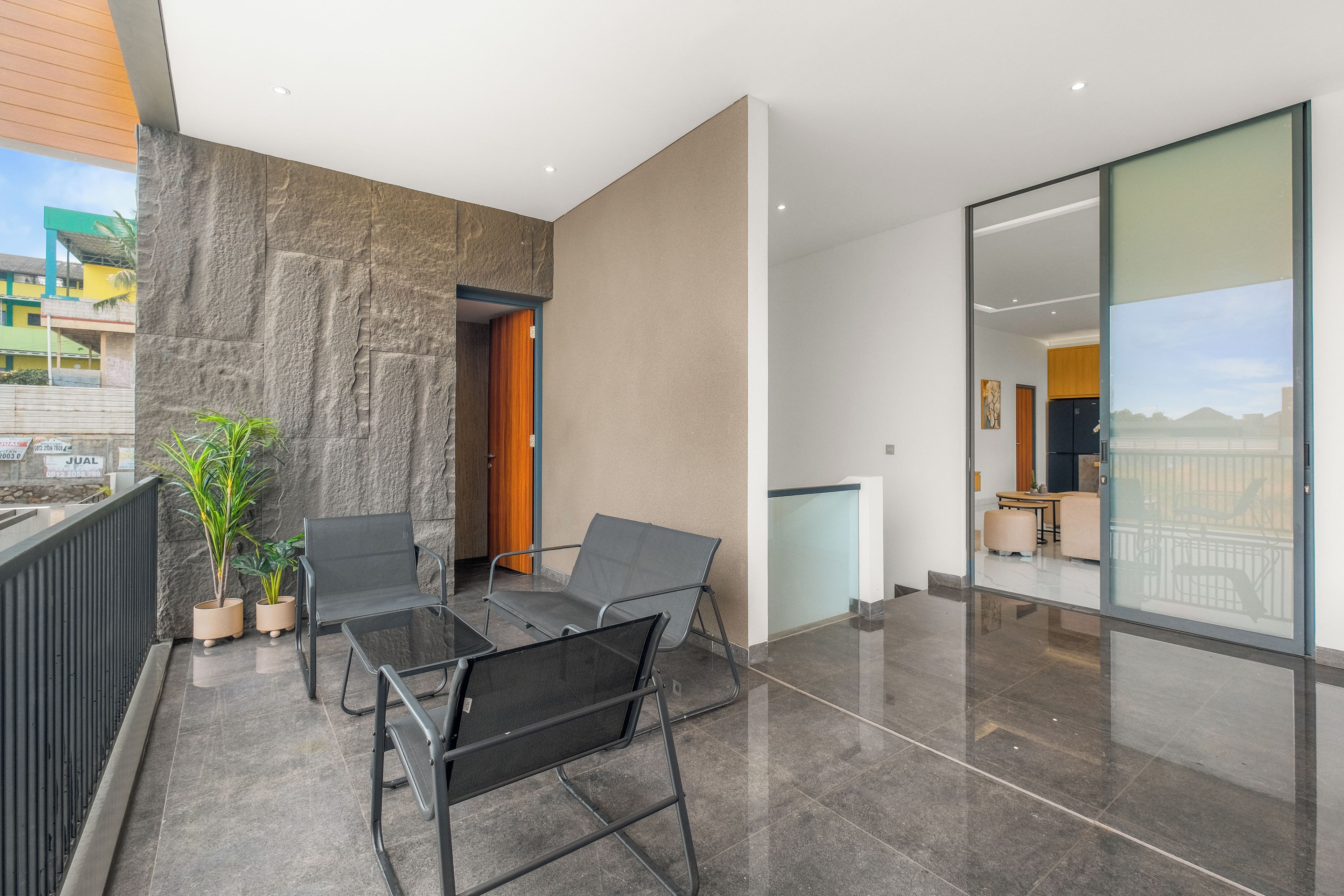 Un balcón moderno con puerta de cristal que da a un comedor, una planta en maceta y vistas de un paisaje urbano.