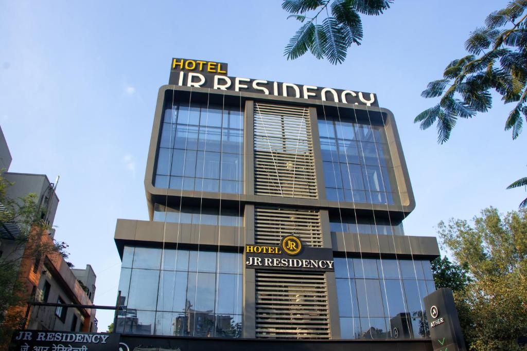 Un moderno edificio de hotel con el nombre 'Hotel JR Residency' visible en la fachada.