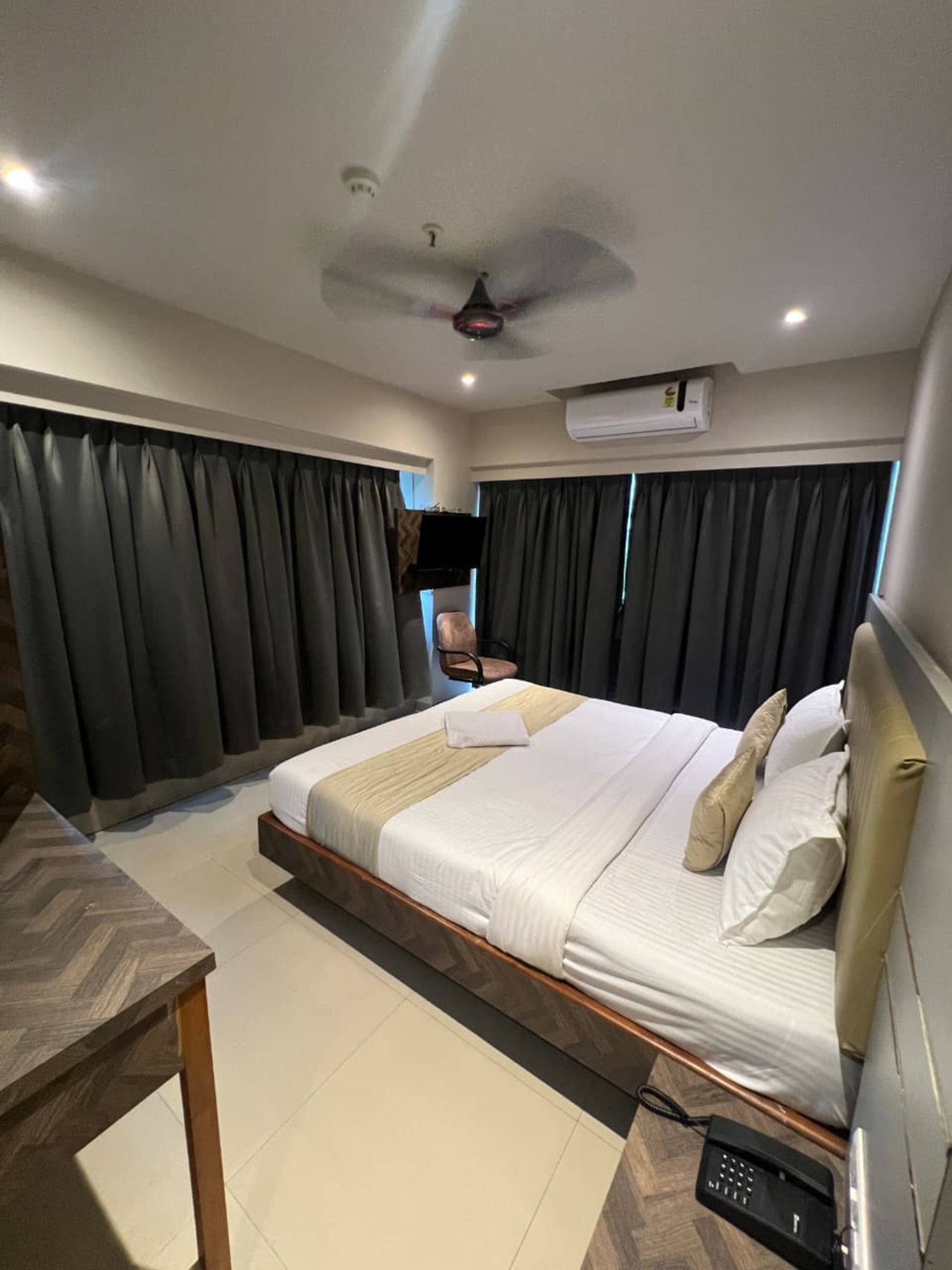 A hotel room with a bed, a desk, an air conditioning unit, and a ceiling fan.