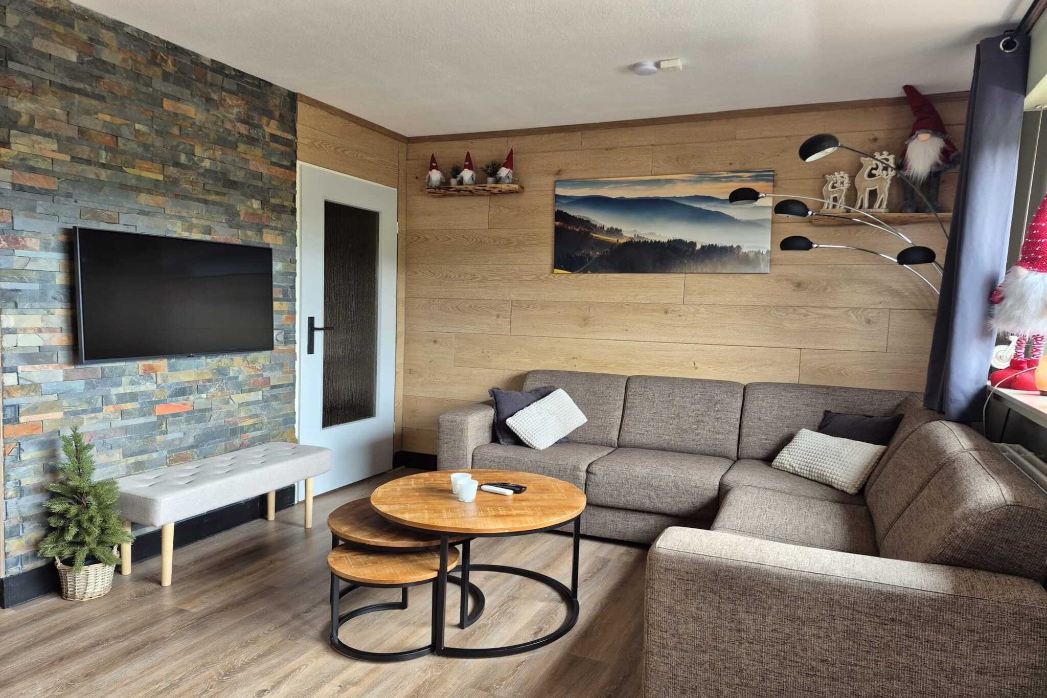 Ein modernes Wohnzimmer mit Steinwand, Flachbildfernseher, einer Couch, einem Couchtisch und einer kleinen Pflanze.