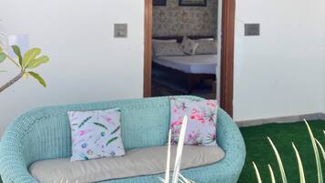 Een kamer met een groene paraplu, een bank met bloemkussens en uitzicht op een slaapkamer door een geopende deur.