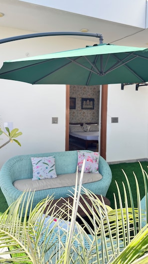A room with a green umbrella, a sofa with floral cushions, and a glimpse of a bed in the background. - Cozy 1-bedroom on a rooftop in a bungalow Jaipur with terrace garden (Jaipur)