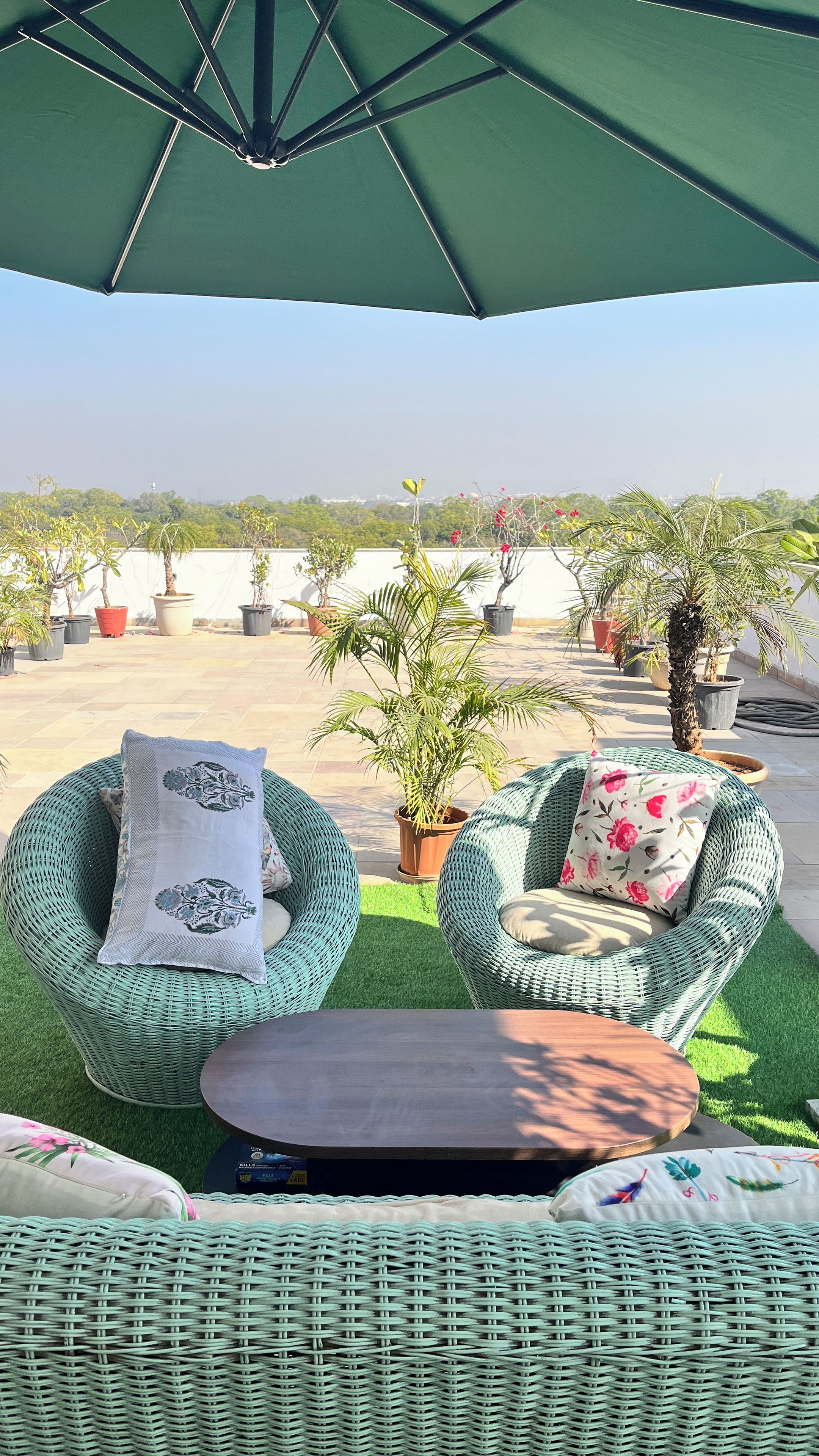 Un espace extérieur aménagé avec des meubles en osier, une table et un parasol vert.