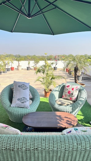 Uma área de estar ao ar livre com móveis de vime, uma mesa e um guarda-sol verde.