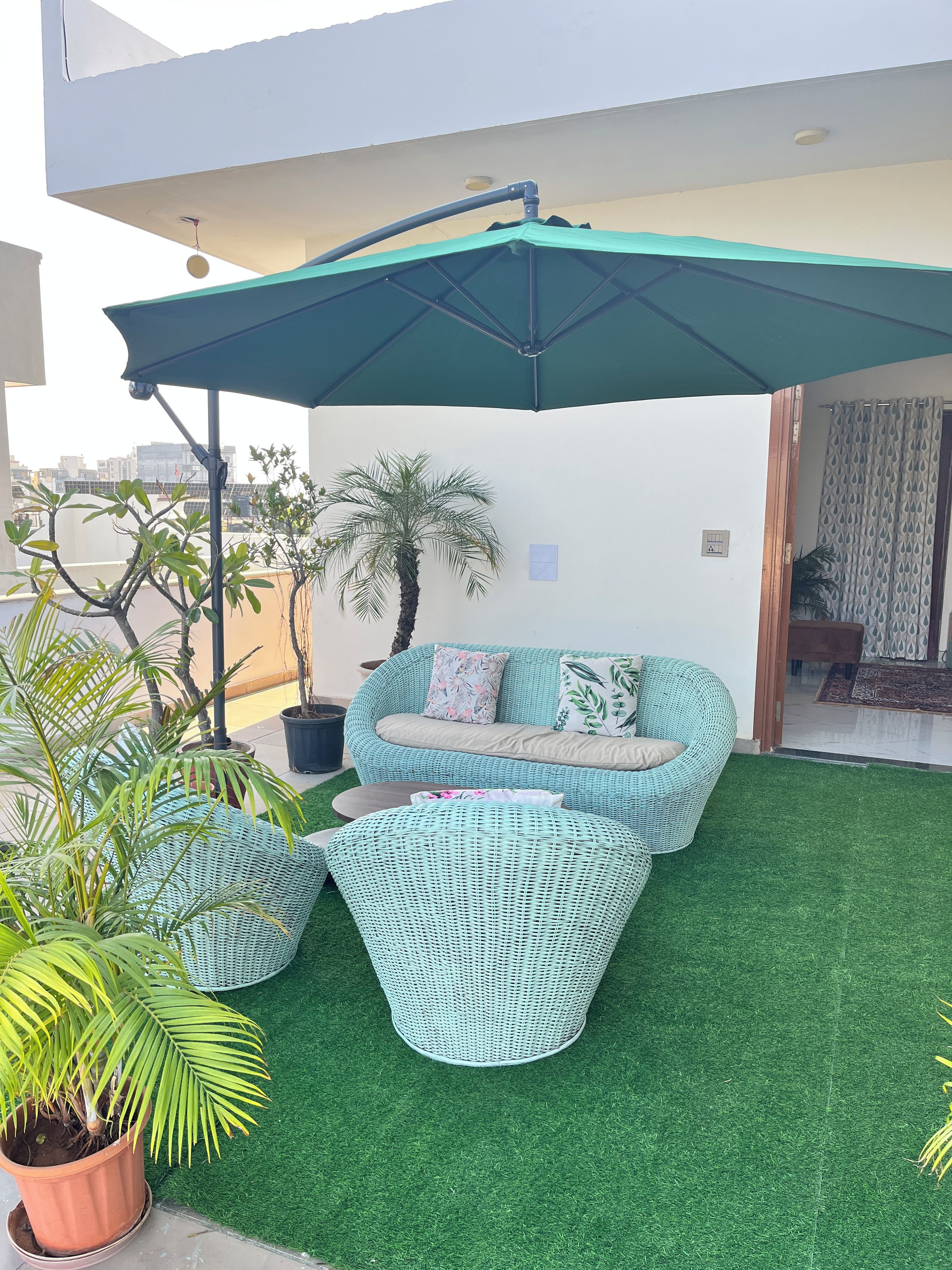 Een terras op het dak met een grasveld van kunstgras, een rieten loungeset en een grote parasol voor schaduw.