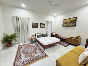 A hotel room with a bed, a sofa, a chair, a small table, a potted plant, and a painting on the wall. - Cozy 1-bedroom on a rooftop in a bungalow Jaipur with terrace garden (Jaipur)