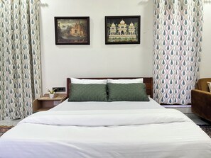 A hotel room with a bed, two framed pictures on the wall, a nightstand, and curtains. - Cozy 1-bedroom on a rooftop in a bungalow Jaipur with terrace garden (Jaipur)