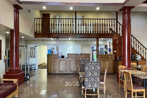 Eine großzügige Lobby mit einer Rezeption, einer Treppe und einem Essbereich mit Holzbänken und einer gemusterten Tischdecke.