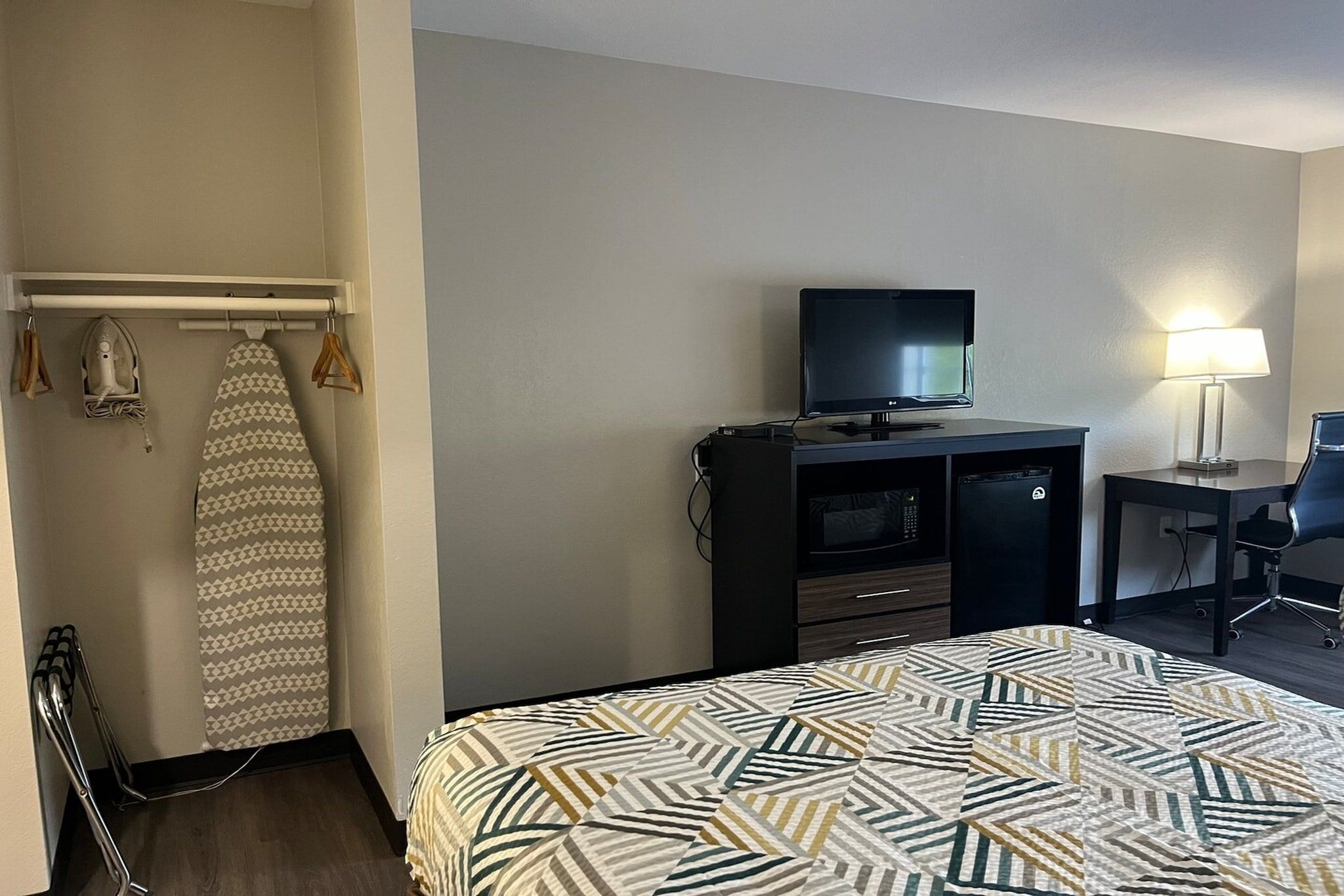 A hotel room with a bed, a desk, a television, and a lamp.