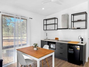 A modern kitchen with a wooden table, white chairs, and black cabinetry. - Villa 1 @ North Peak - A one bedroom villa for two (Pokolbin)