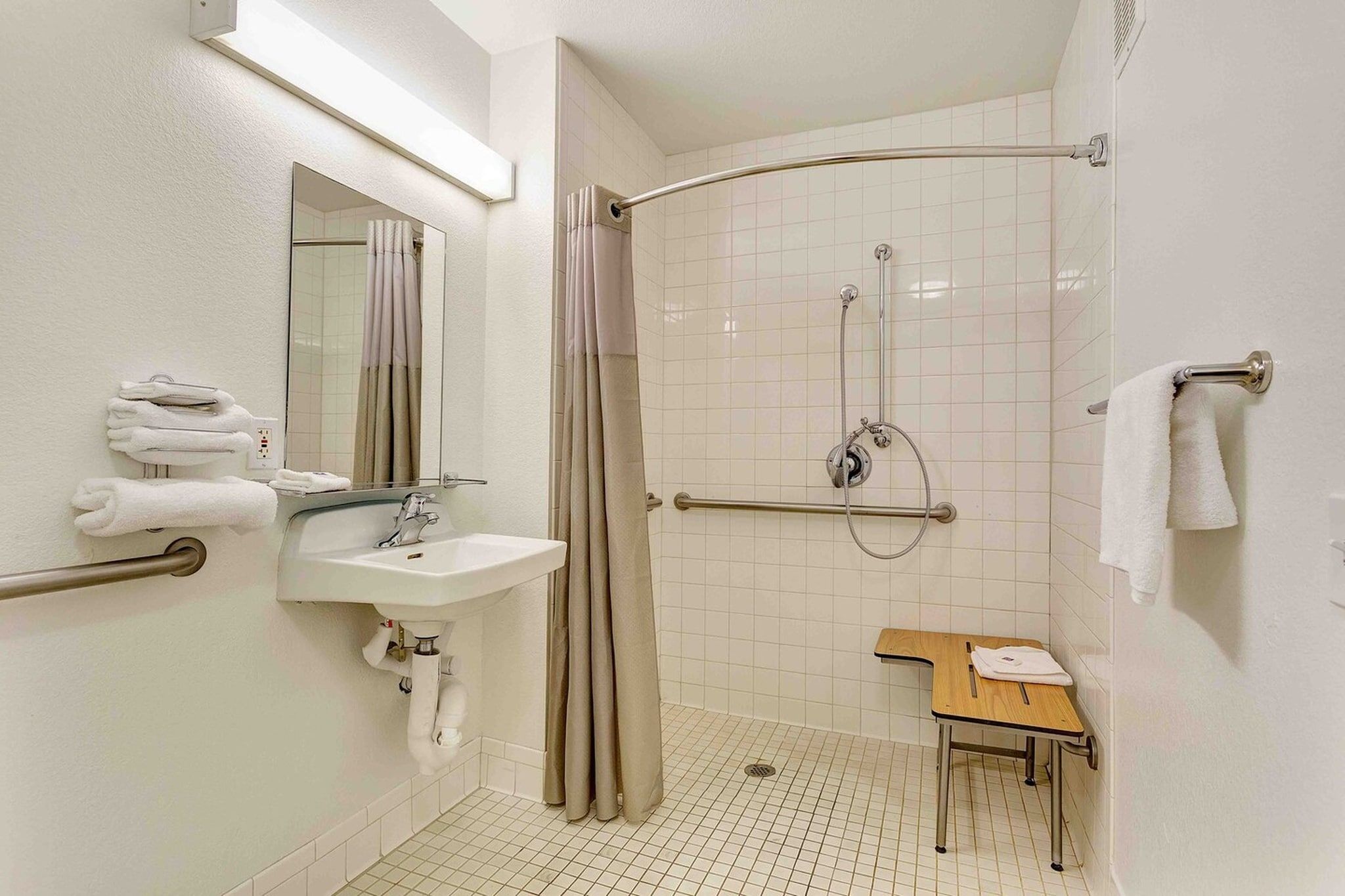 A bathroom with a shower, sink, mirror, towel rack, and a small wooden table.
