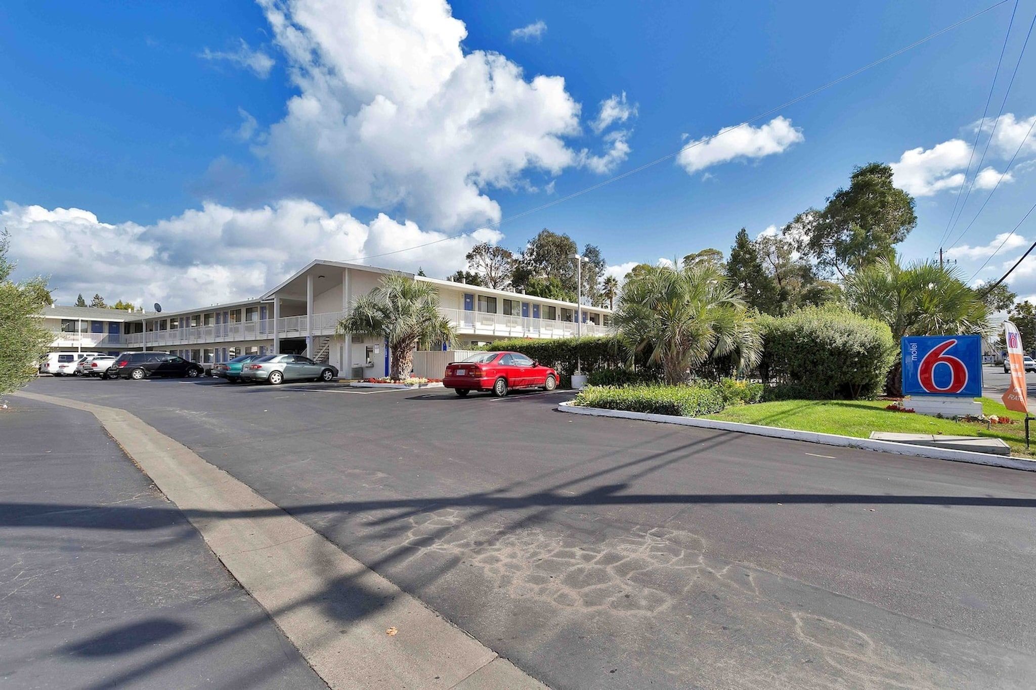A motel with a parking lot, a red car parked in front, and a sign indicating the motel number.