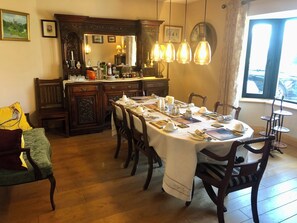 A dining area with a long table set for a meal, wooden chairs, a vintage cabinet, and hanging light fixtures. - Family run boutique self-catering house, with homemade baking on arrival. (Doneraile, Co Cork)