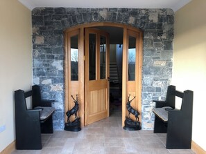 A wooden door with glass panels, flanked by two black chairs with a deer's head design, leading to a room with a stone wall.