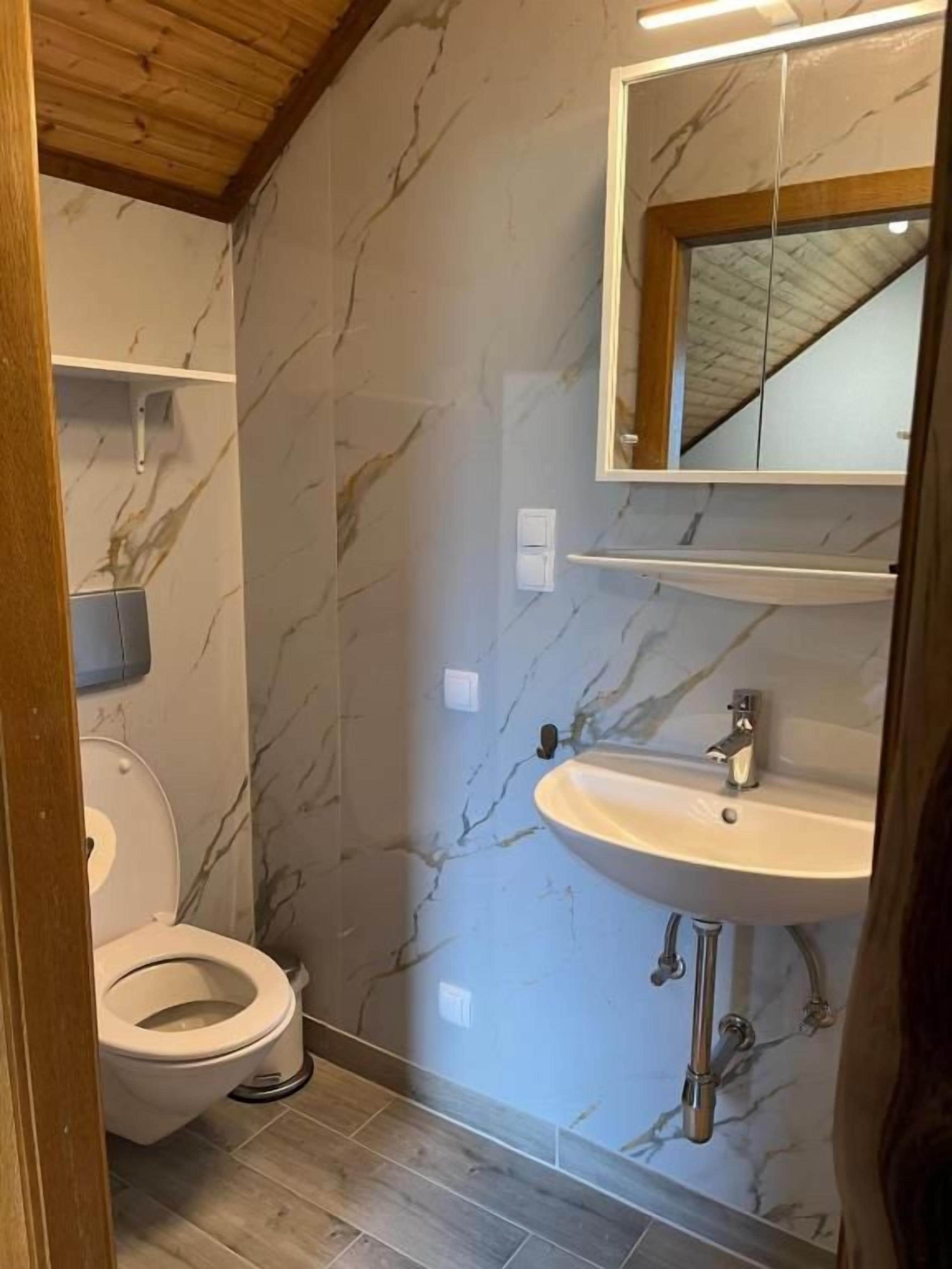 Un baño con pared de mármol, lavamanos blanco y un inodoro.