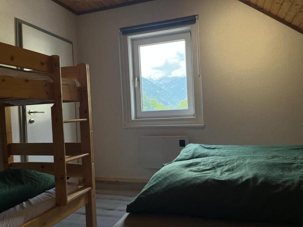 A room with a bunk bed, a window with a mountain view, and a door.