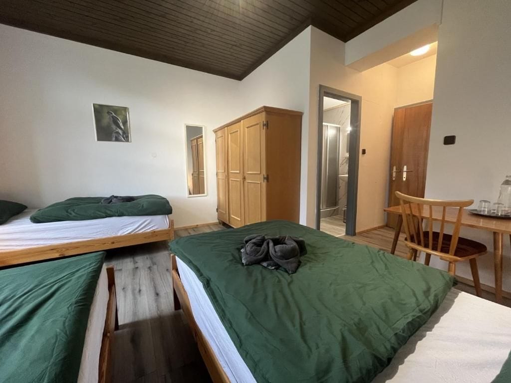 A bedroom with two beds, a wooden wardrobe, a desk with a chair, and a door leading to a bathroom.
