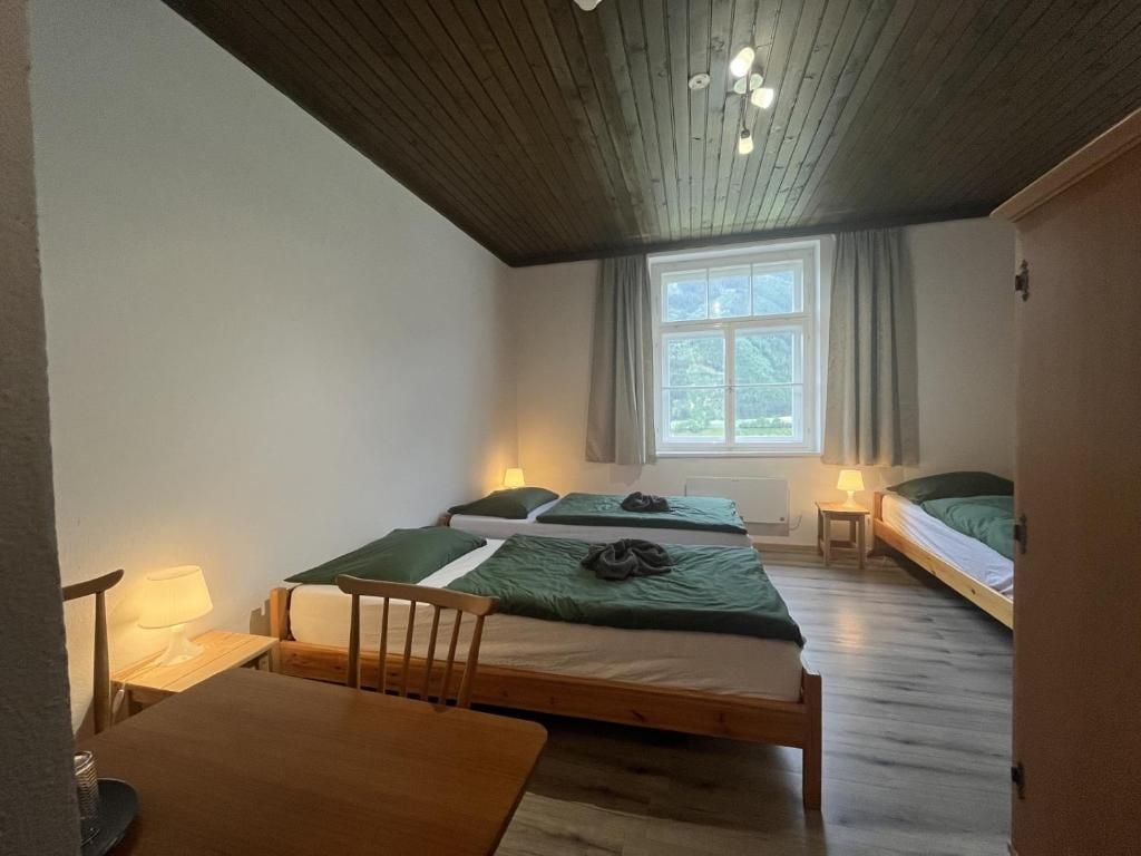 Quarto com três camas de solteiro, uma mesa de madeira e uma janela com cortinas.