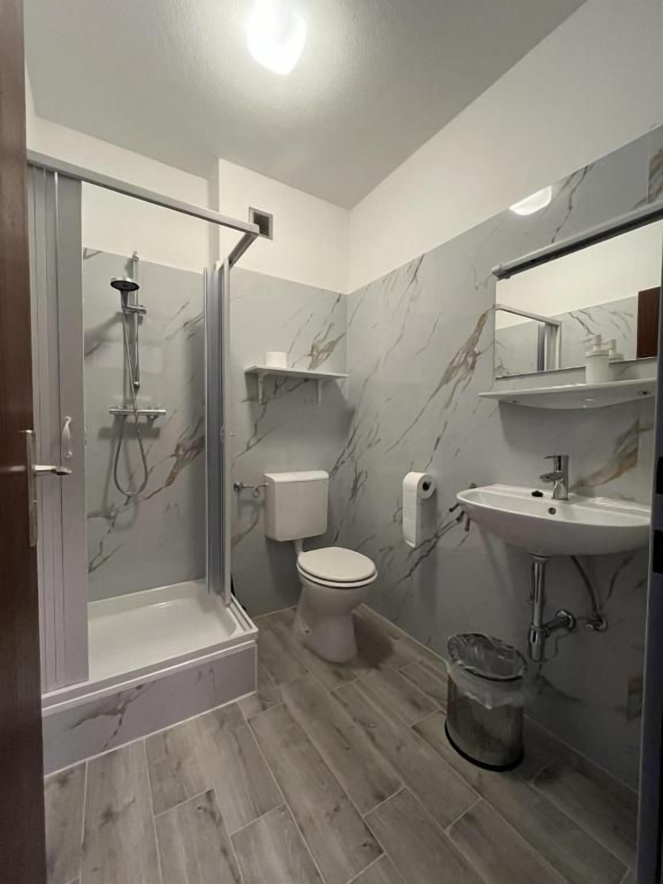 A bathroom with a shower, toilet, sink, and marble walls.