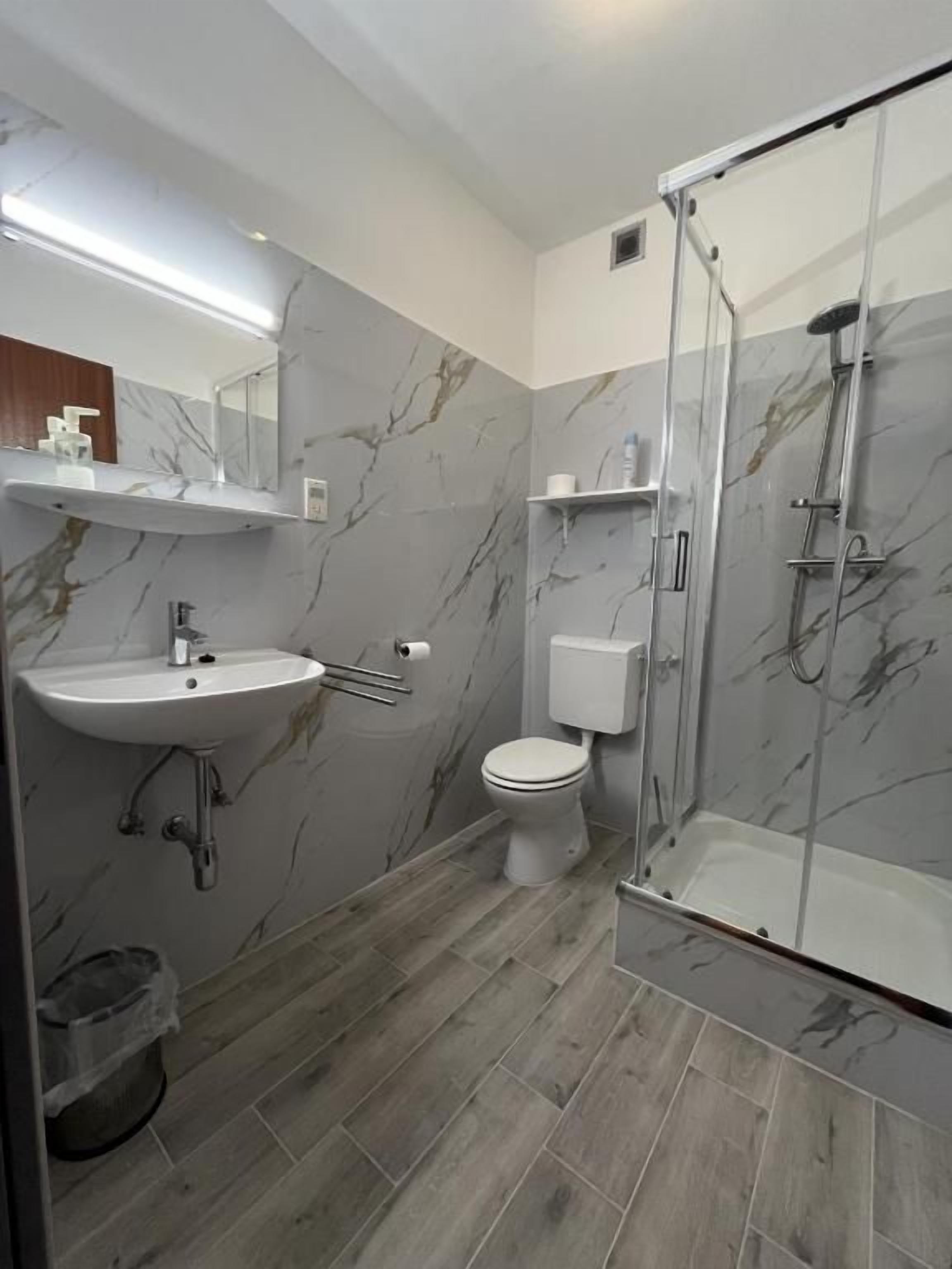 Ein modernes Badezimmer mit Marmorverkleidung, einem Waschbecken, einer Toilette und einer Duschkabine.