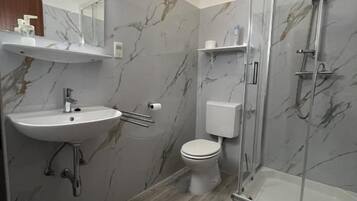 Ein modernes Badezimmer mit Marmorverkleidung, einem Waschbecken, einer Toilette und einer Duschkabine.