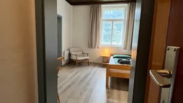 Et værelse med en seng, en stol, et vindue med gardiner samt et loft med træbjælker og lamper.