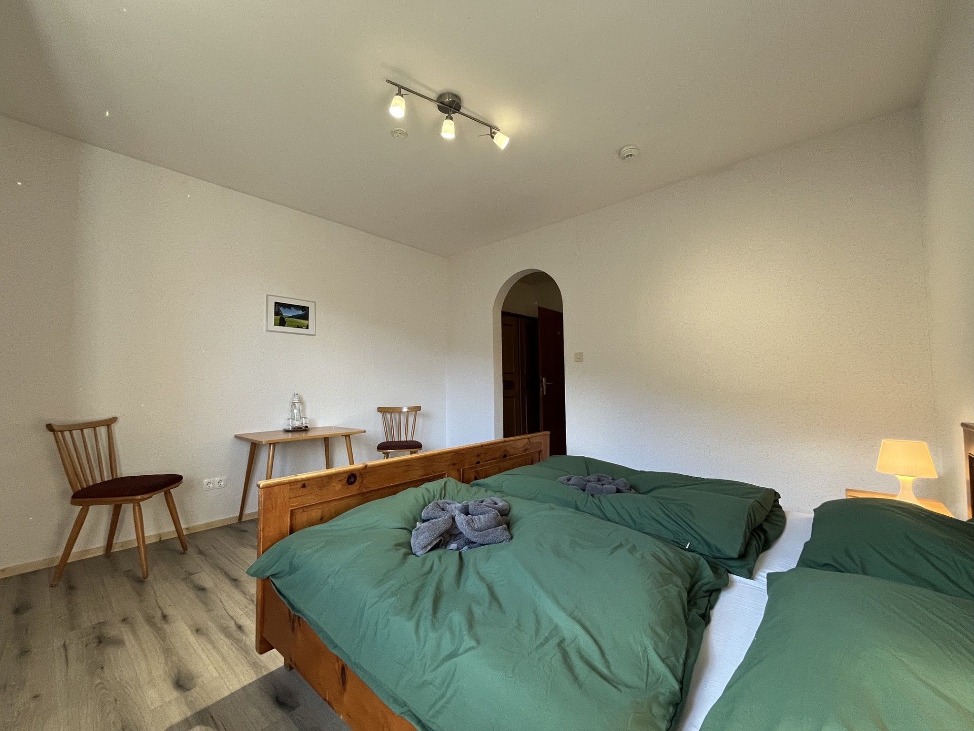 Ein Schlafzimmer mit zwei Betten, einem Holzsessel, einem kleinen Tisch und einem Bild an der Wand.