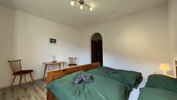 Ein Schlafzimmer mit zwei Betten, einem Holzsessel, einem kleinen Tisch und einem Bild an der Wand.