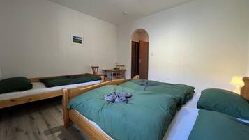 A room with two wooden beds, a small table with chairs, and a door leading to another room.