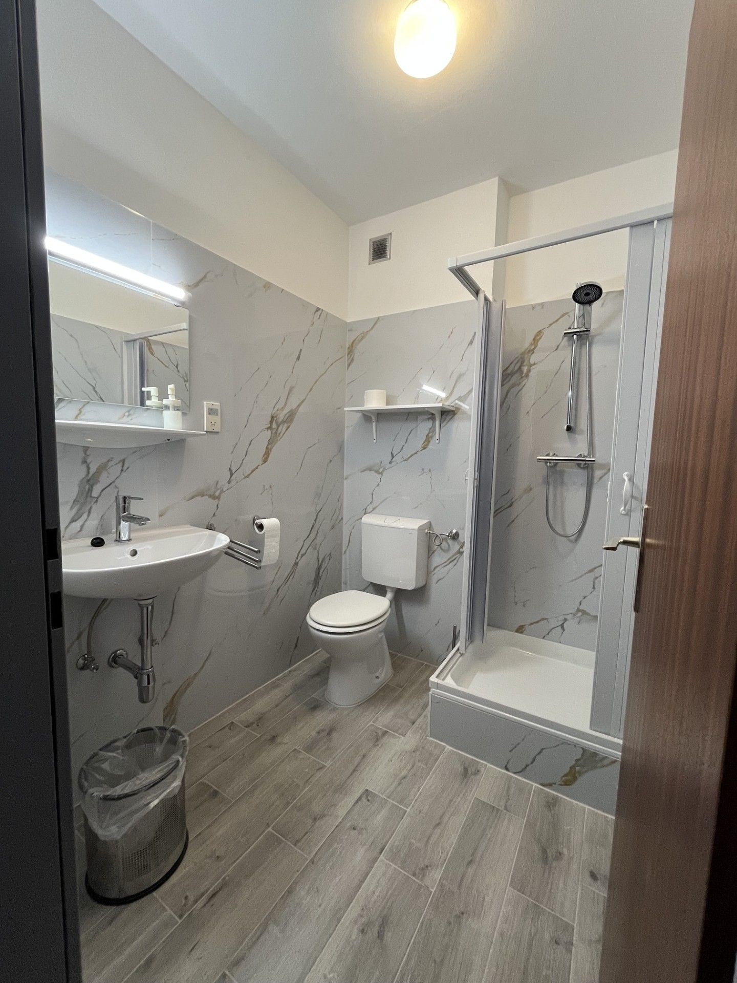 Une salle de bain moderne avec un pare-baignoire en marbre, des toilettes, un lavabo et une douche.