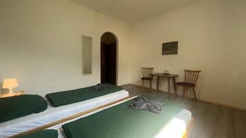 A room with two single beds, a small table, two chairs, and a door leading to another room.