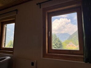 A room with two windows, one of which offers a view of a mountain landscape and a building.