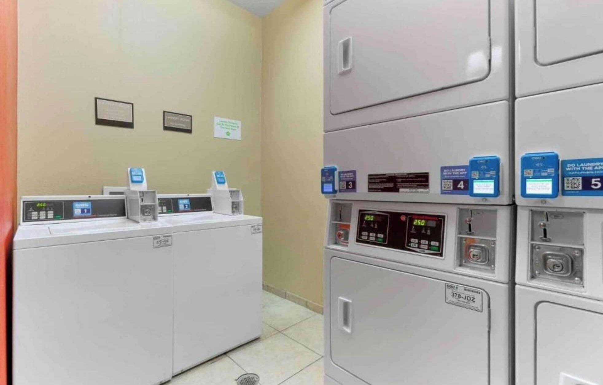 Une laverie équipée de plusieurs machines à laver et de plusieurs séchoirs, chacun doté d’un panneau de commande et d’un code QR pour accéder aux services numériques.