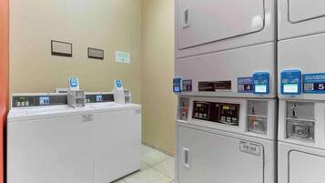 Une laverie équipée de plusieurs machines à laver et de plusieurs séchoirs, chacun doté d’un panneau de commande et d’un code QR pour accéder aux services numériques.