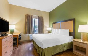 A hotel room with a bed, two bedside tables with lamps, a desk with a television, and a window with curtains.