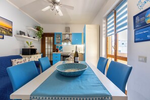 A modern kitchen with blue cabinets, a dining table with blue chairs, and a ceiling fan. - 100 meters from the beach (Alghero)