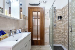 A bathroom with a wooden door, a glass shower enclosure, and a white sink with a mirror above it. - 100 meters from the beach (Alghero)