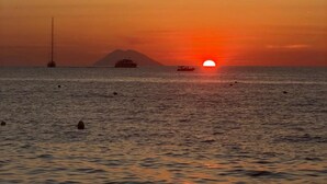 Ein Sonnenuntergang über einem ruhigen Meer mit einem Segelboot und einem Schiff in der Ferne.