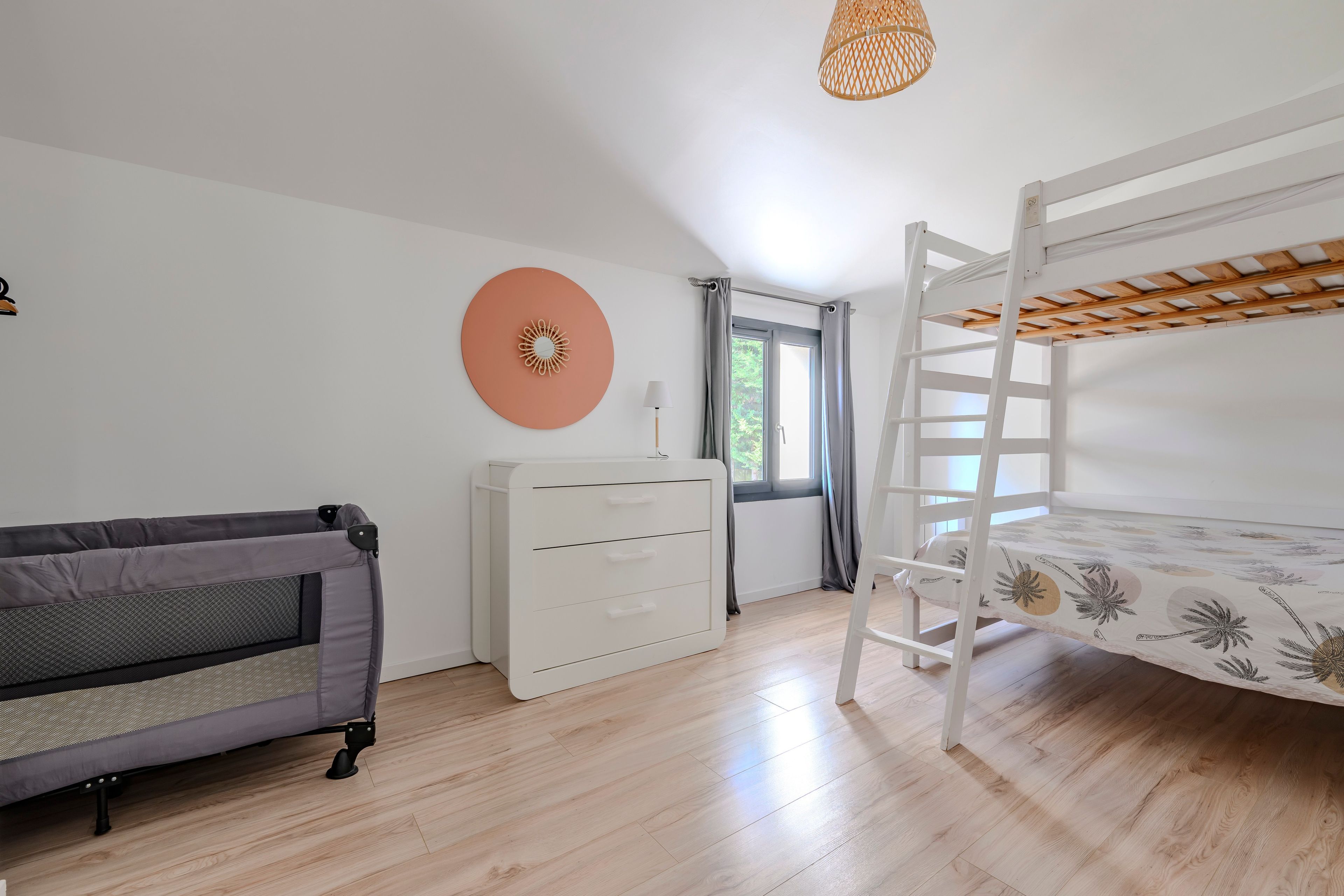 Quarto de criança com beliche, sofá, cômoda e janela com cortinas.