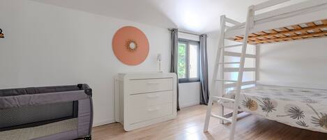 Quarto de criança com beliche, sofá, cômoda e janela com cortinas.