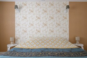 Une chambre avec un papier peint à motifs, un lit recouvert d’une couvre-lit à motifs géométriques, deux lampes de chevet et une table de chevet blanche.