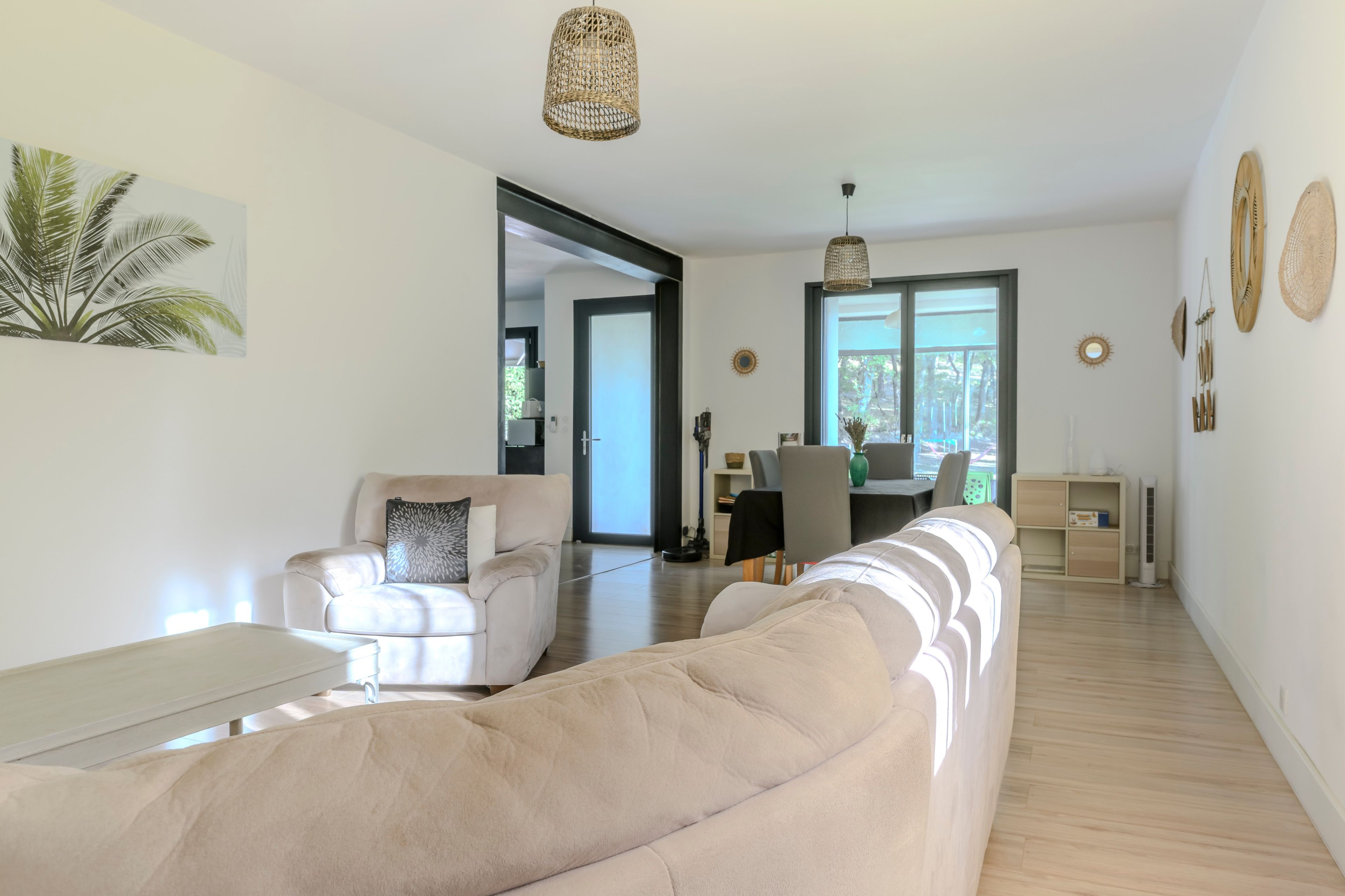 En moderne stue med en beige sofa, et sofabord og et spiseområde med bord og stole.