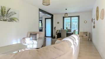 En moderne stue med en beige sofa, et sofabord og et spiseområde med bord og stole.