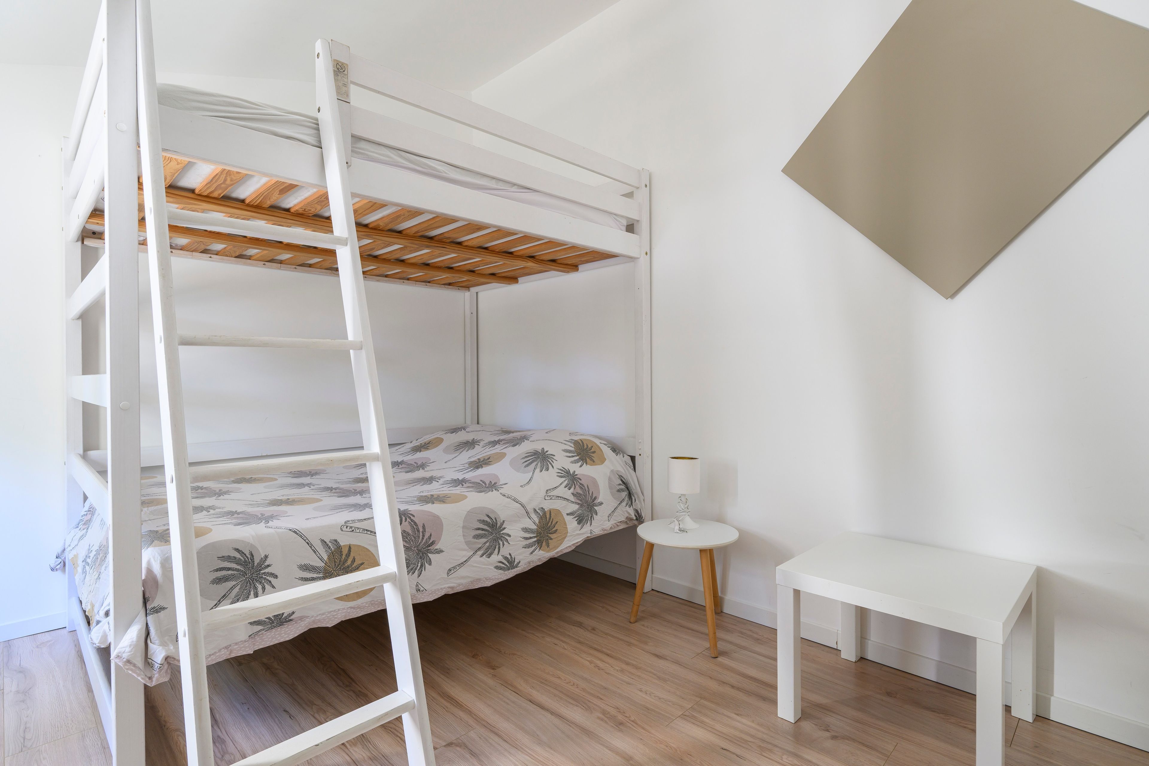 A bunk bed with a ladder, a small bedside table, and a wall-mounted lamp.