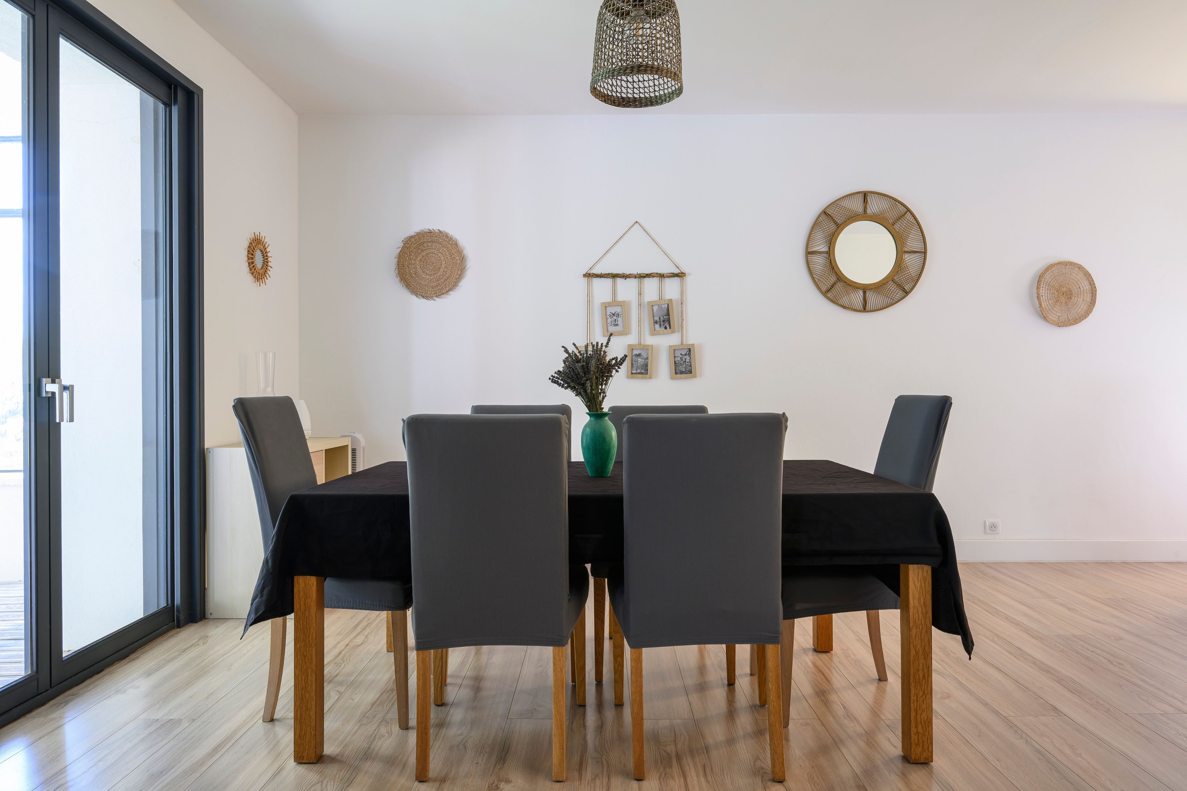 Un coin repas avec une table dressée pour quatre personnes, entourée de chaises recouvertes de housses sombres.