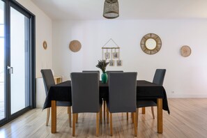 Un coin repas avec une table dressée pour quatre personnes, entourée de chaises recouvertes de housses sombres.