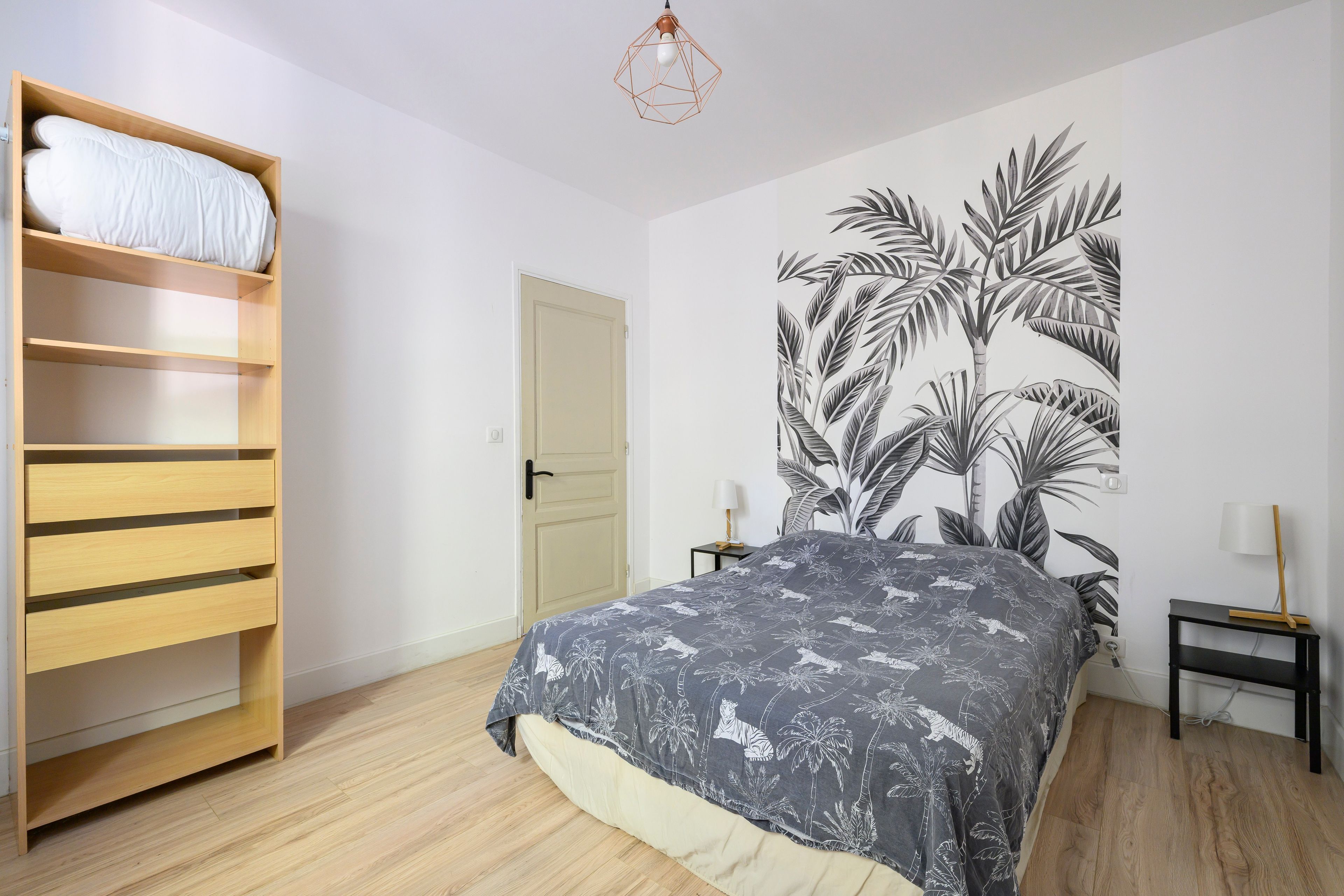A bedroom with a bed, a wardrobe, a door, and a wall with a leaf pattern.