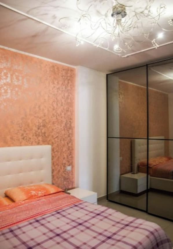 Ein Schlafzimmer mit einem Bett, einem Nachttisch, einem Spiegel und einer Schiebetür.