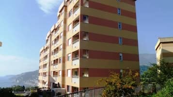A multi-story residential building with balconies, located in a hilly area with a clear sky.