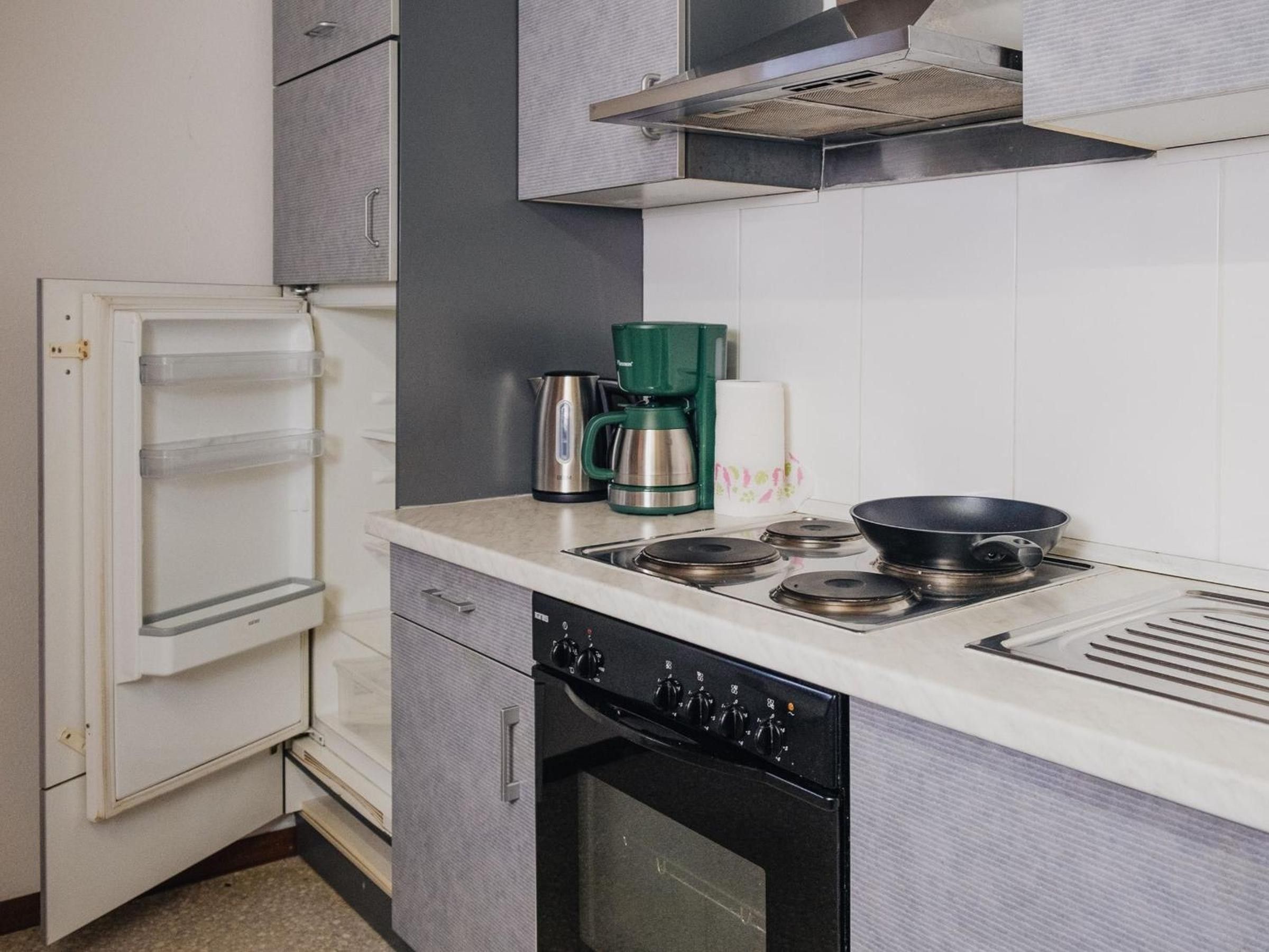 Una cocina compacta con un refrigerador integrado, estufa y cafetera.